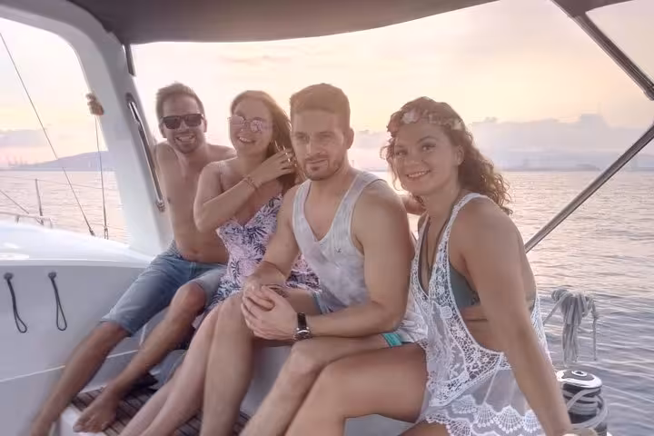 Friends relaxing on a Barcelona sailing tour at sunset, enjoying open bar drinks and onboard snacks