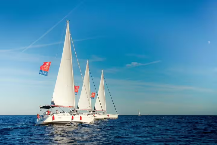 Sailboats with white sails cruise together off the coast of Barcelona on a clear Mediterranean day sailing tour