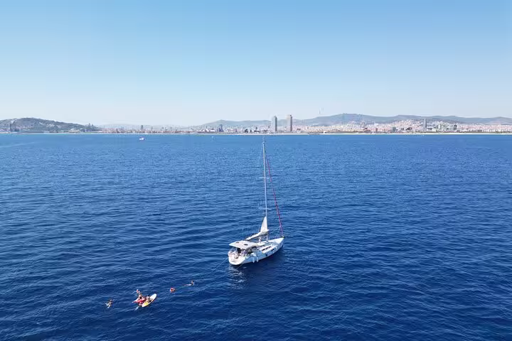 Sailboat floating on the sparkling Mediterranean Sea near Barcelona's skyline, offering a small group sailing experience with snacks and cava.