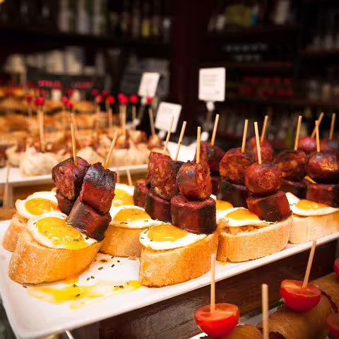 Assorted tapas with sausages and eggs on crusty bread in a traditional Barcelona tavern, highlighting local culinary delights.