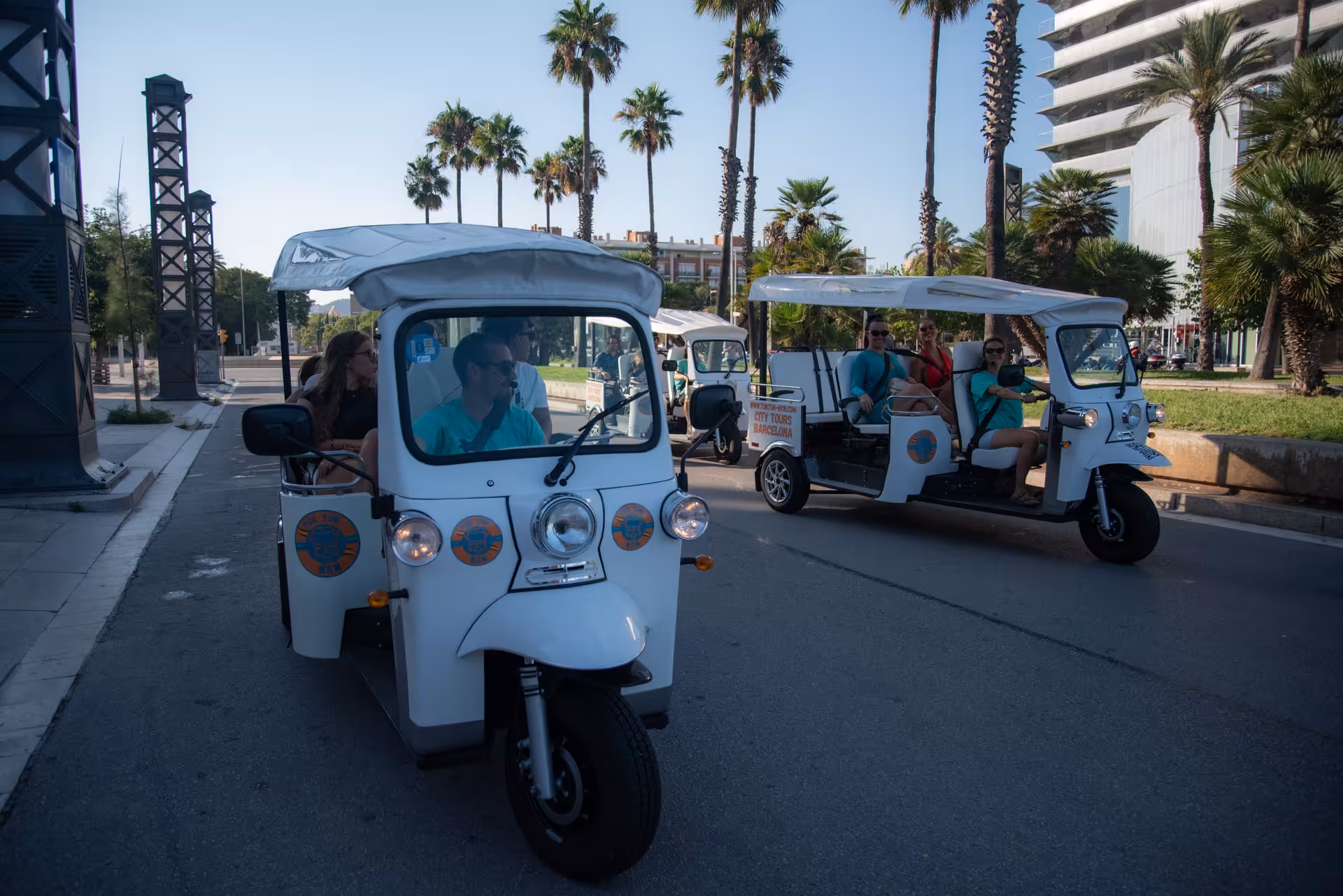 Barcelona tuk tuk convoy on a full city highlights tour, cruising a palm-lined avenue near the waterfront