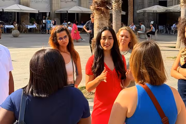 Tour guide in red dress leads group on immersive walking tour in sunny Barcelona plaza.