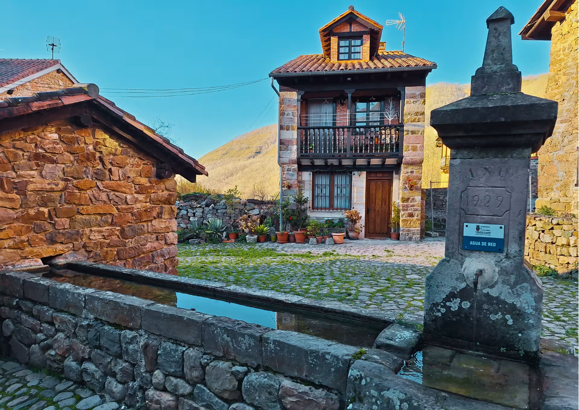 Historic stone fountain dated 1929 beside traditional Cantabrian house in Bárcena Mayor village day trip
