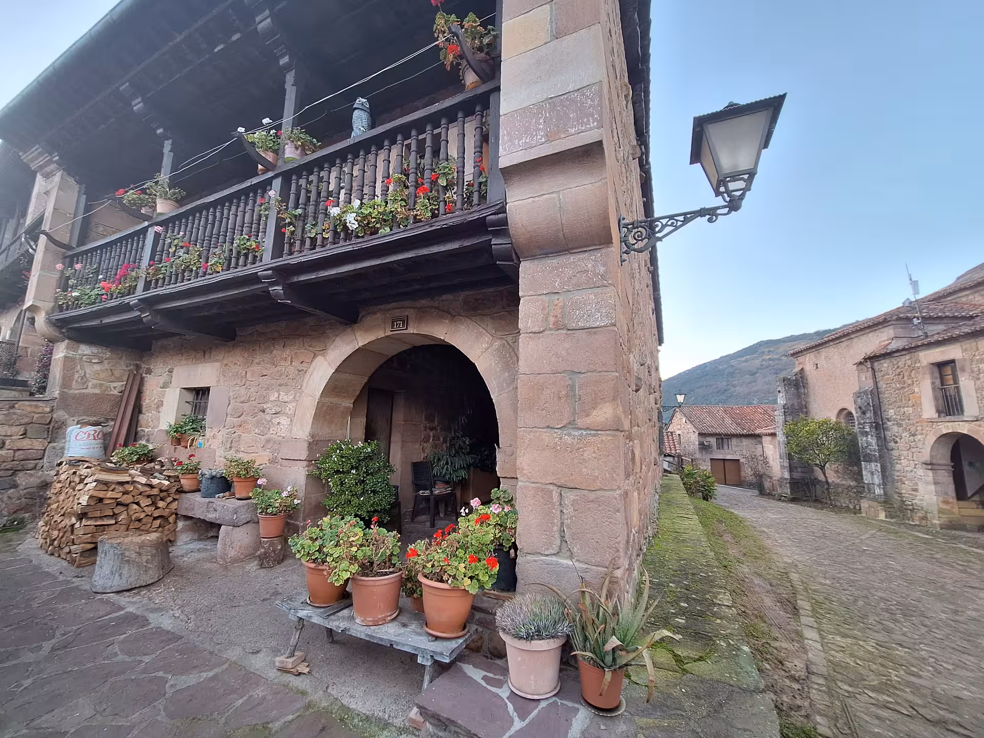 Historic stone house with wooden balcony adorned with colorful flowers in Barcena Mayor Cantabria village day trip