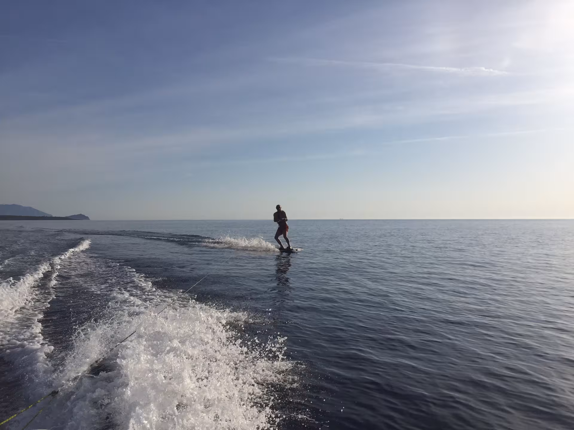 Silhouette of wakeboarder on serene waters in Bari Sardo, offering an exhilarating water sports lesson under clear skies.