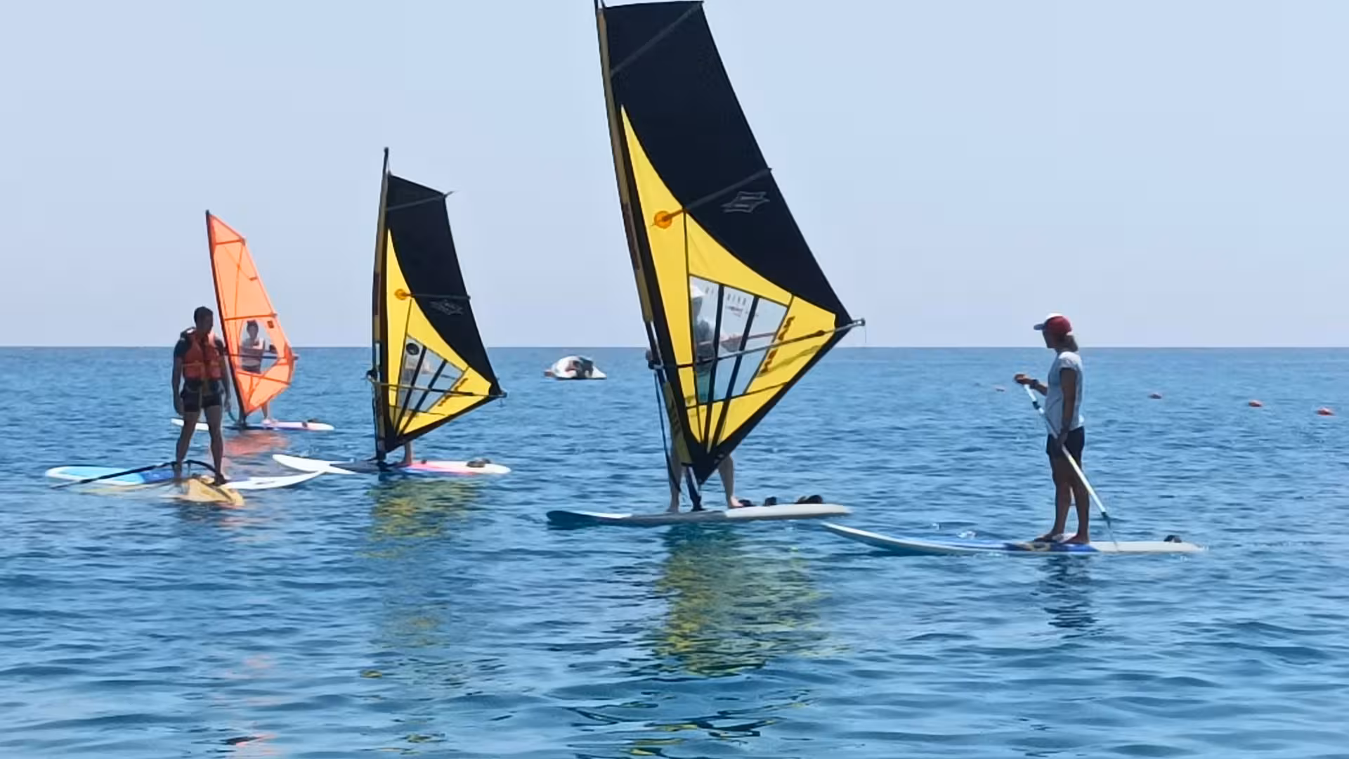 Group of windsurfers in Bari Sardo engaging in a basic windsurf course on clear blue waters, perfect for beginners.