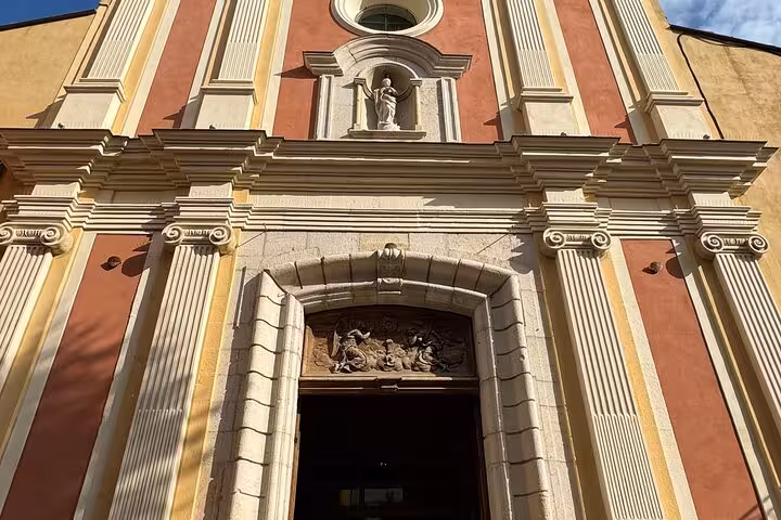 Baroque church facade with ornate white stone details and red walls in Eze, French Riviera