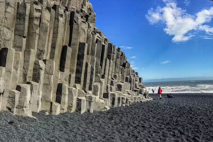 Black sand beach with towering basalt columns on Iceland's South Coast with tourists exploring the shoreline