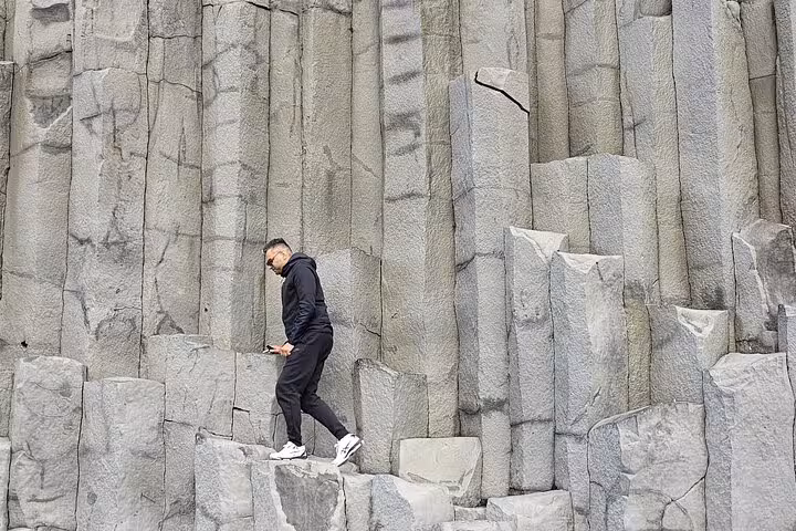 Tourist walking on basalt column rock formations on Iceland's South Coast