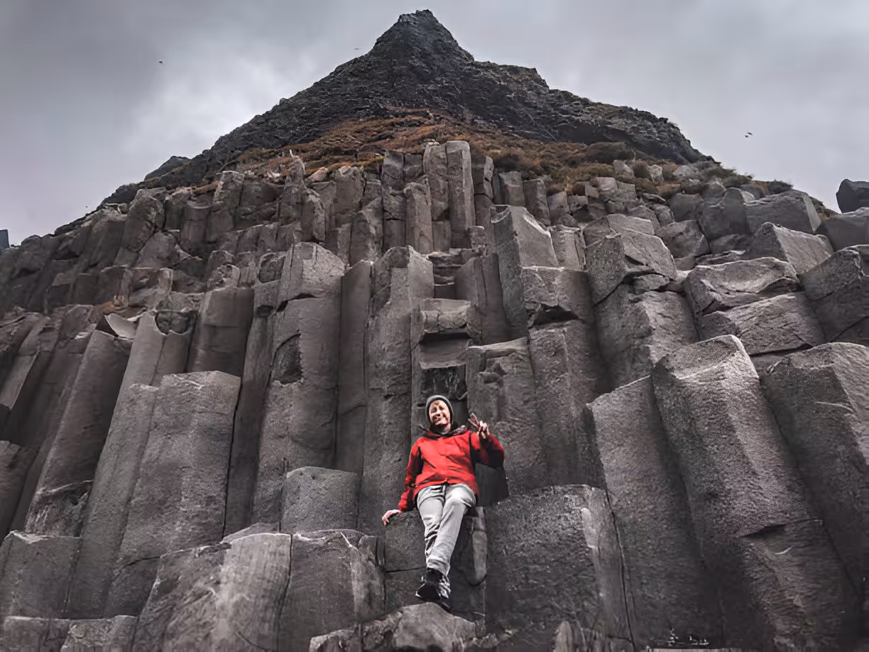 Traveler in red hoodie sitting among basalt rock columns on Iceland's south coast