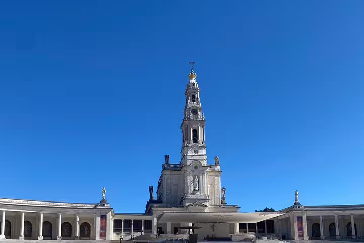 The majestic Basilica of Our Lady of the Rosary at the Sanctuary of Fátima under a clear blue sky, showcasing its grandeur.