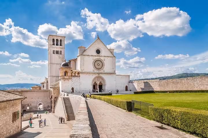 The Basilica of Saint Francis in Assisi, showcasing its grand facade and lush surroundings on a sunny day tour.