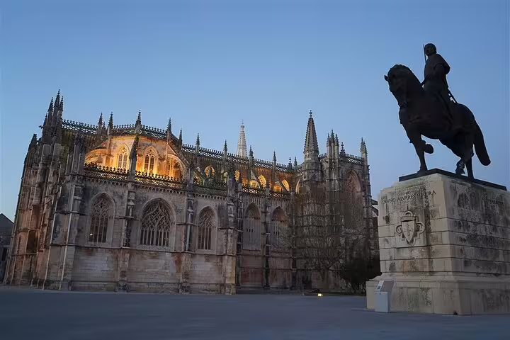 Batalha Monastery illuminated at dusk with an equestrian statue, featured in a 3-day Portugal World Heritage tour from Lisbon.
