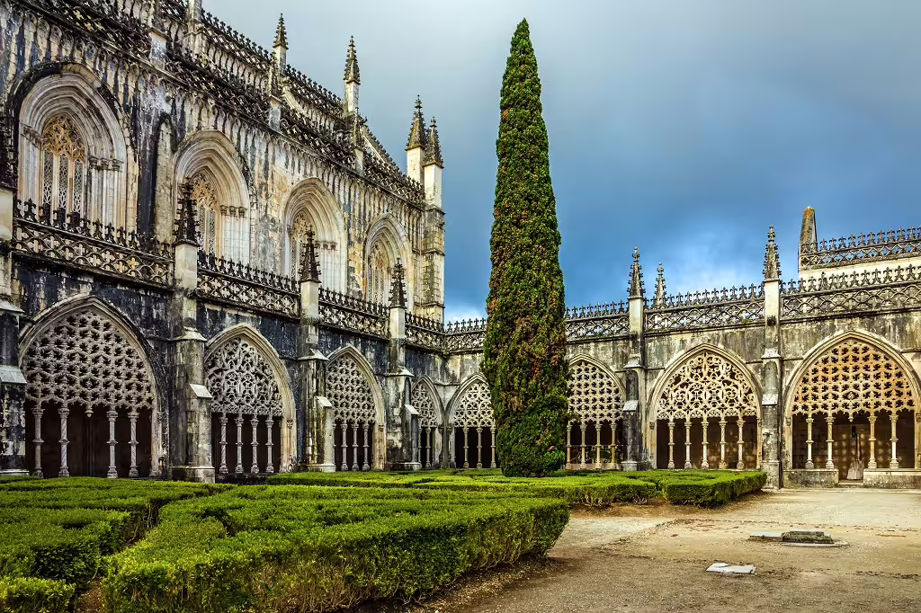 Gothic architecture of Batalha Monastery in Portugal with intricate stonework and lush garden, perfect for cultural tours.