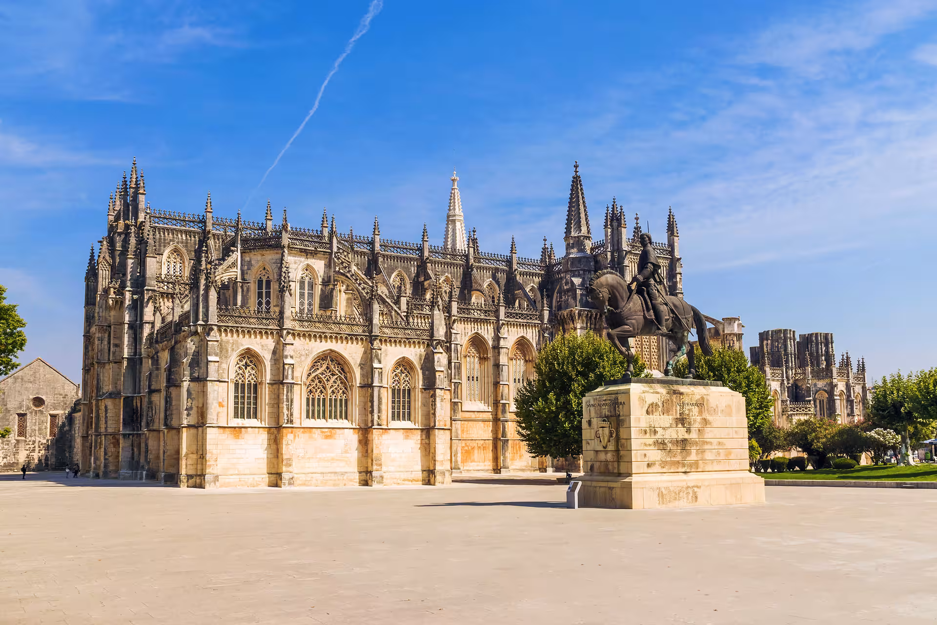 Batalha Monastery's intricate Gothic architecture with a historic equestrian statue, set against a clear blue sky.
