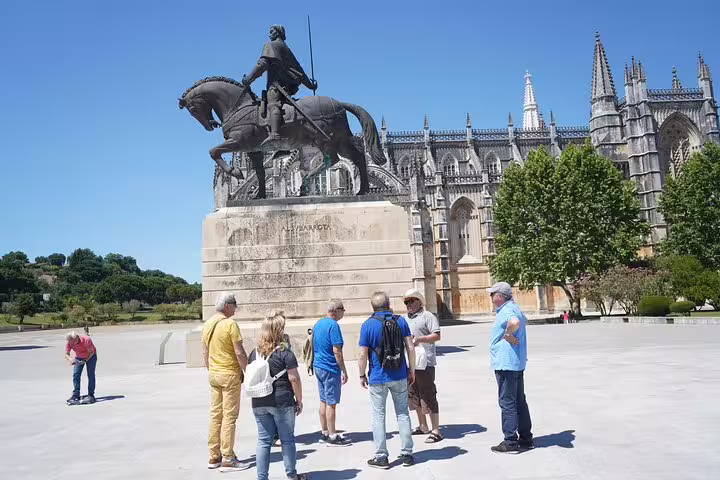 Tourists explore the iconic Batalha Monastery and equestrian statue on a sunny day during a private tour from Lisbon.