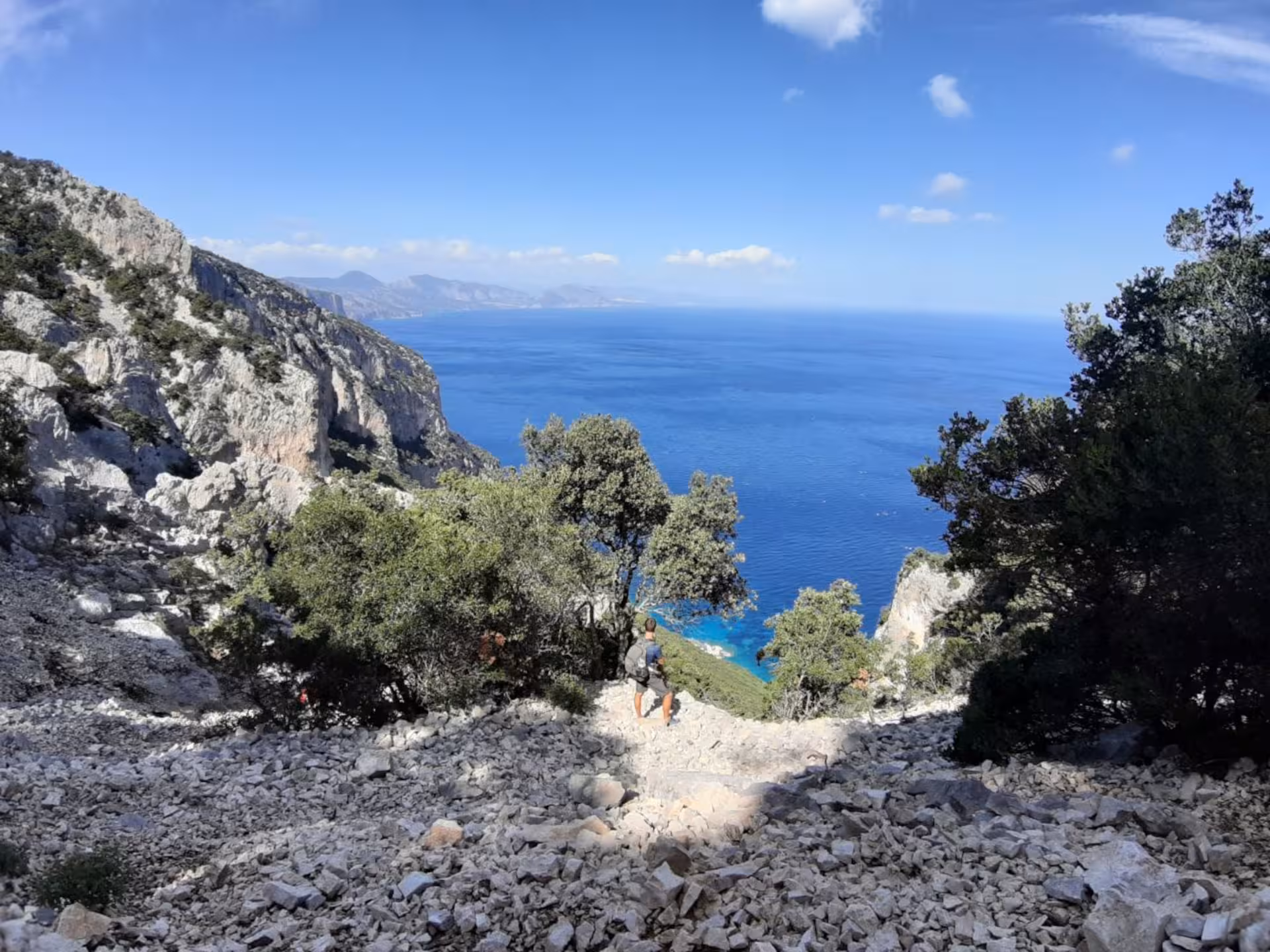 Hiker descending rocky path with stunning Mediterranean Sea view on trek to Cala Mariolu from Baunei.
