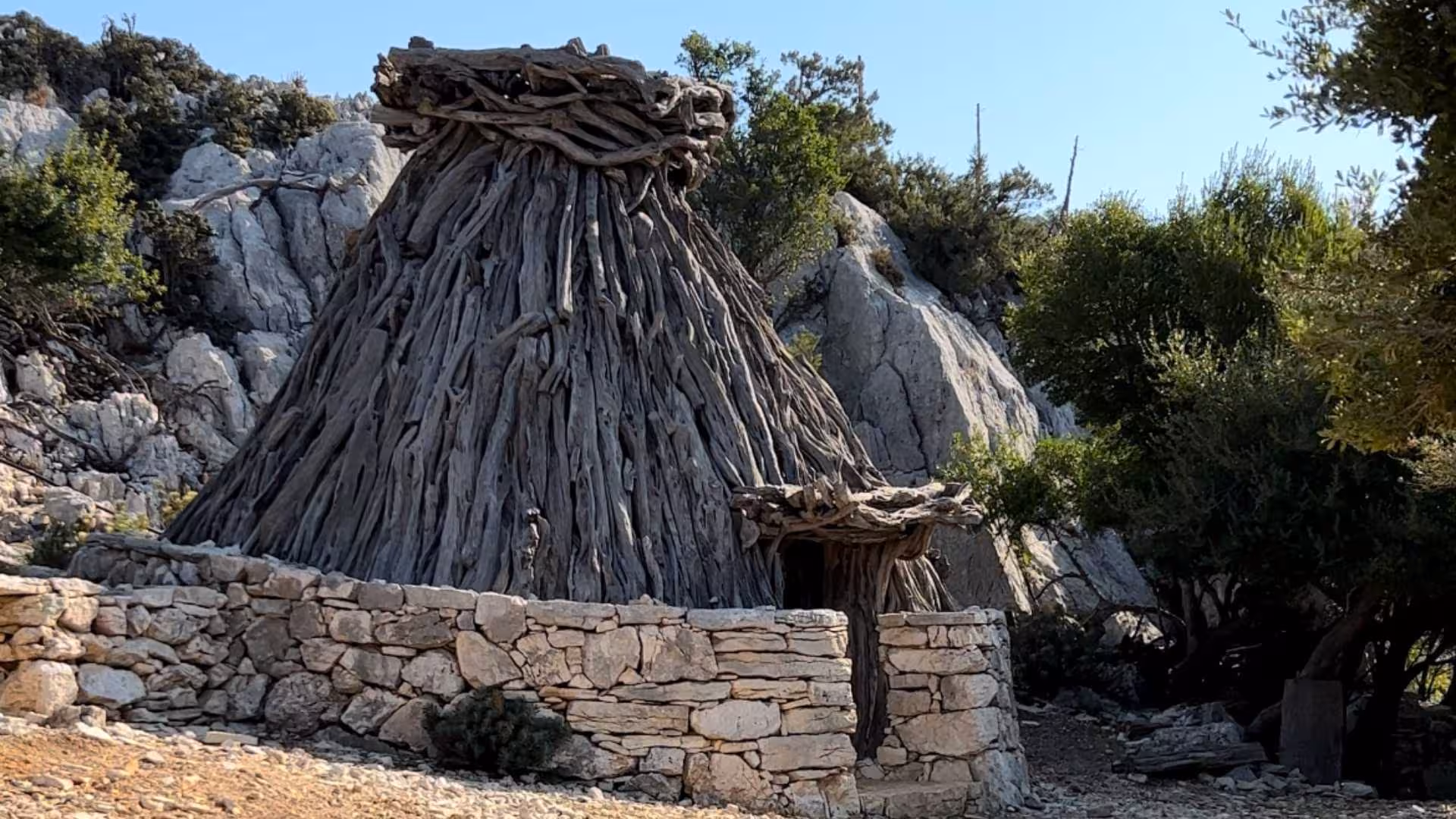 Traditional stone and wood hut nestled among rocky terrain at Punta Salinas, Baunei, on a sunny day.