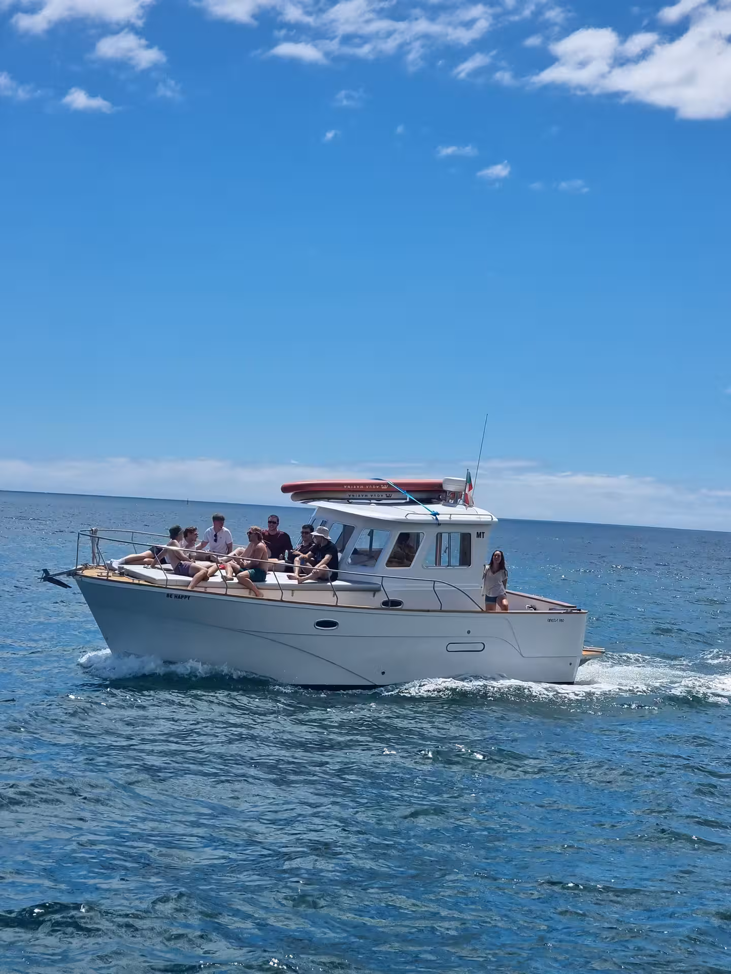 Group enjoying a scenic sunset yacht cruise on the BE HAPPY private charter over clear blue waters.