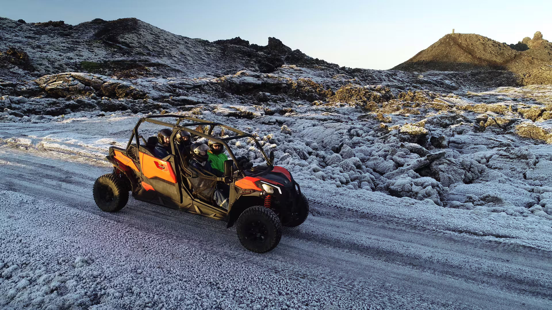 Orange and black beach buggy with passengers driving on snowy lava field volcanic landscape