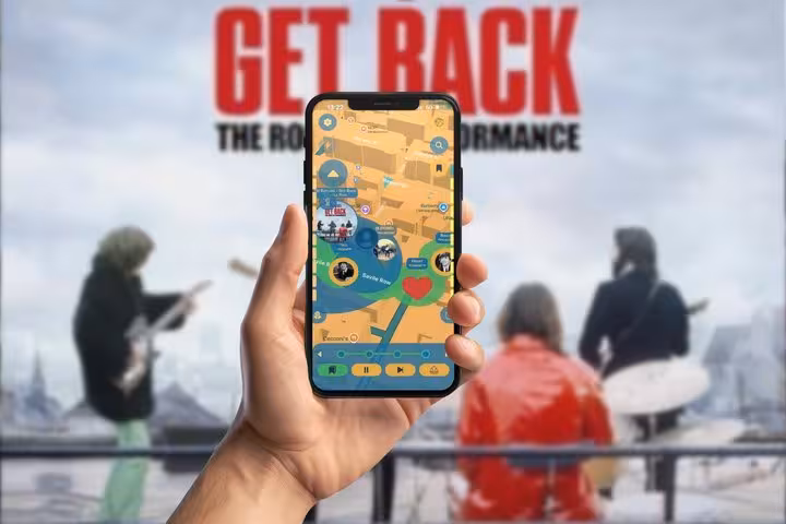 Hand holding smartphone with Beatles walking tour mobile game map, Get Back rooftop concert backdrop