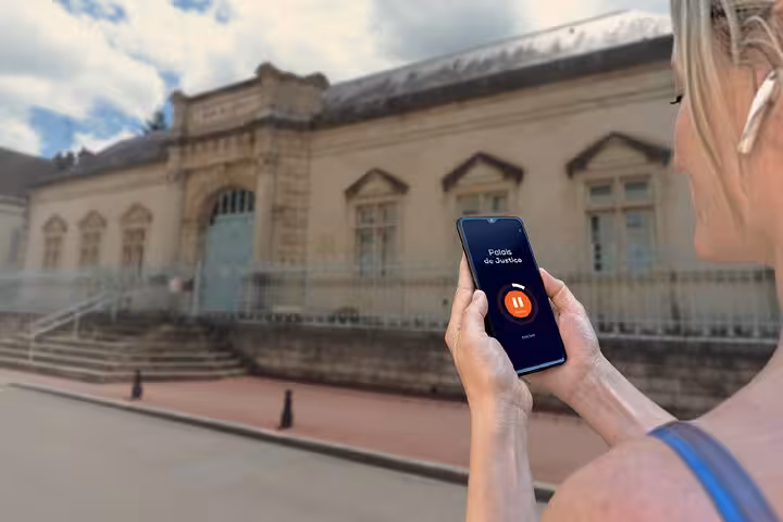 Woman holding smartphone with GPS audio guide app at Palais de Justice in Beaune, France