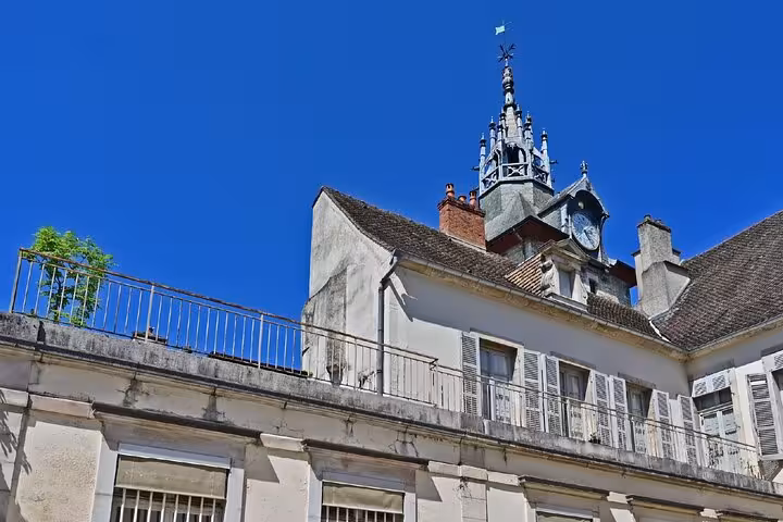 Historic building rooftops and ornate clock tower spire in Beaune, France under blue sky