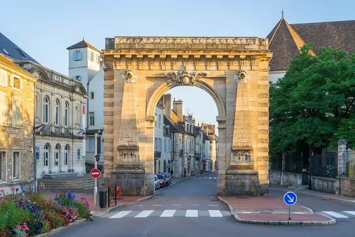 Historic stone arch gate on a quiet street in Beaune, France, with classic buildings and greenery