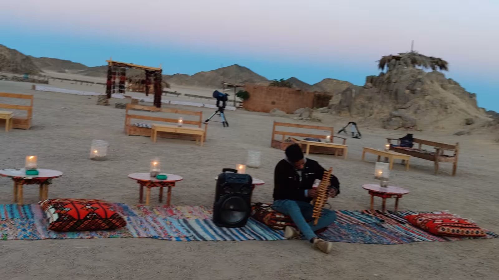 Musician playing instrument at Bedouin desert camp with candles and rugs at dusk in Marsa Alam