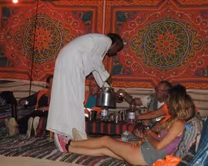 Bedouin host serving tea to tourists inside a traditional decorated camp tent in Marsa Alam
