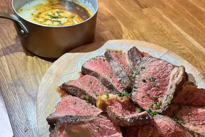 Sliced medium-rare beef with pan sauce on wooden board, from a Marseille cooking class with a local chef