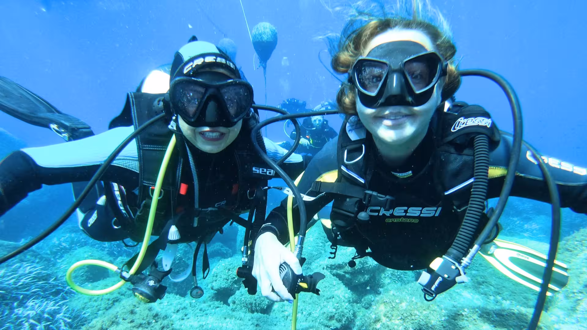 Two beginner divers enjoying an underwater adventure in Cagliari's clear blue sea, part of a scuba diving experience.