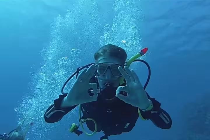 Beginner scuba diver underwater giving OK hand signal in clear blue sea during intro diving experience