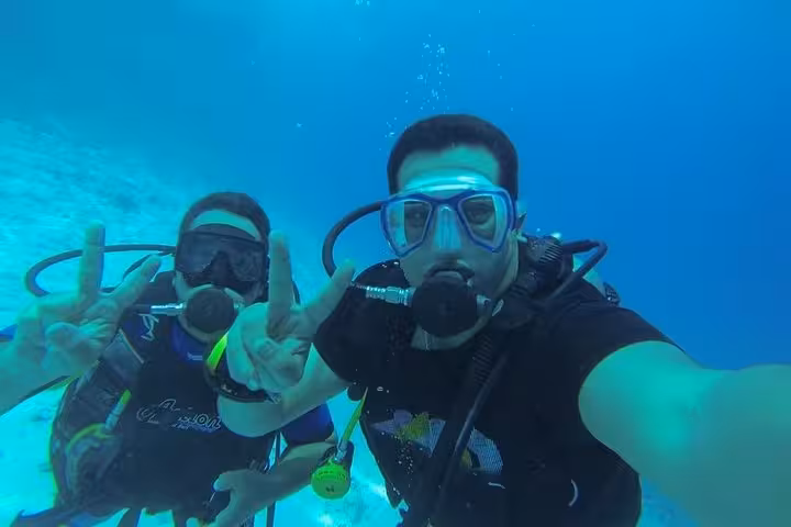 Two beginner scuba divers underwater taking a selfie, practicing hand signals on an intro diving experience
