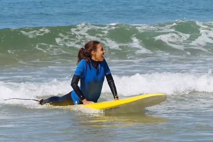 Excited beginner surfer on yellow board enjoying surf lessons at Praia Grande Pera Algarve Portugal