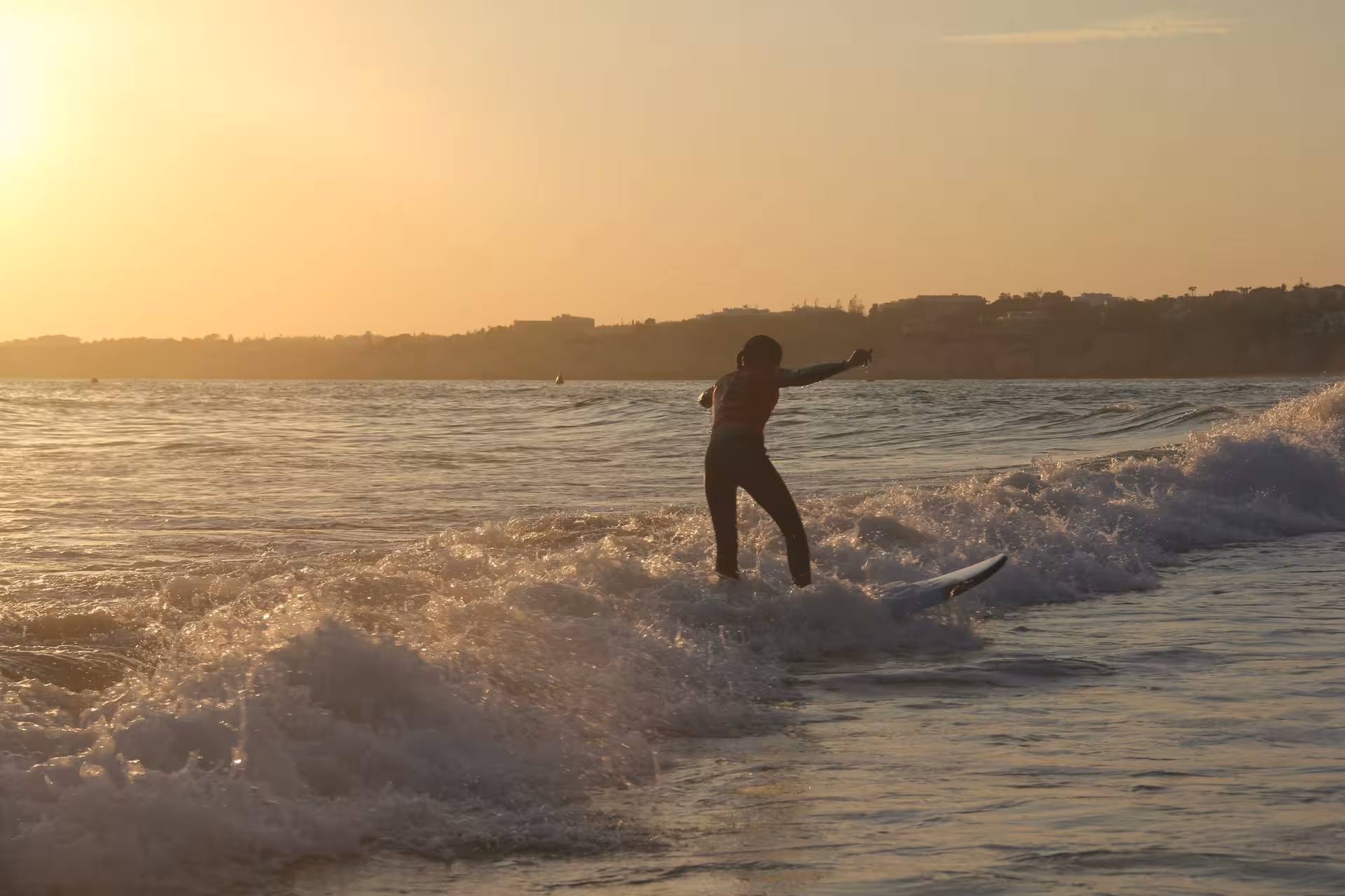 Beginner surfer practicing balance on gentle waves at sunset during a 3-hour group surf course on a scenic beach