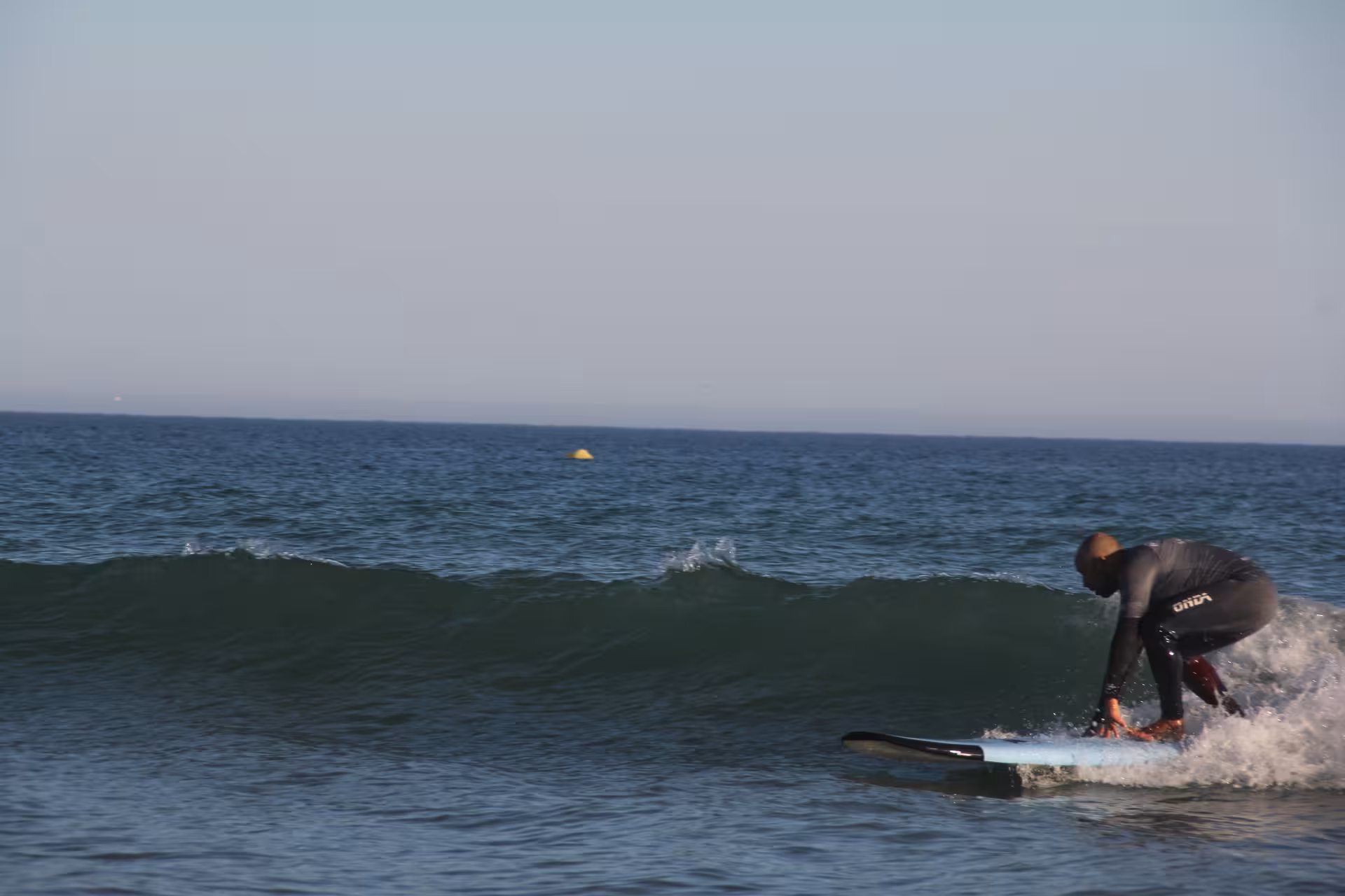 Beginner surfer in wetsuit catching a small wave during a surf lesson clinic on a calm blue ocean at sunset