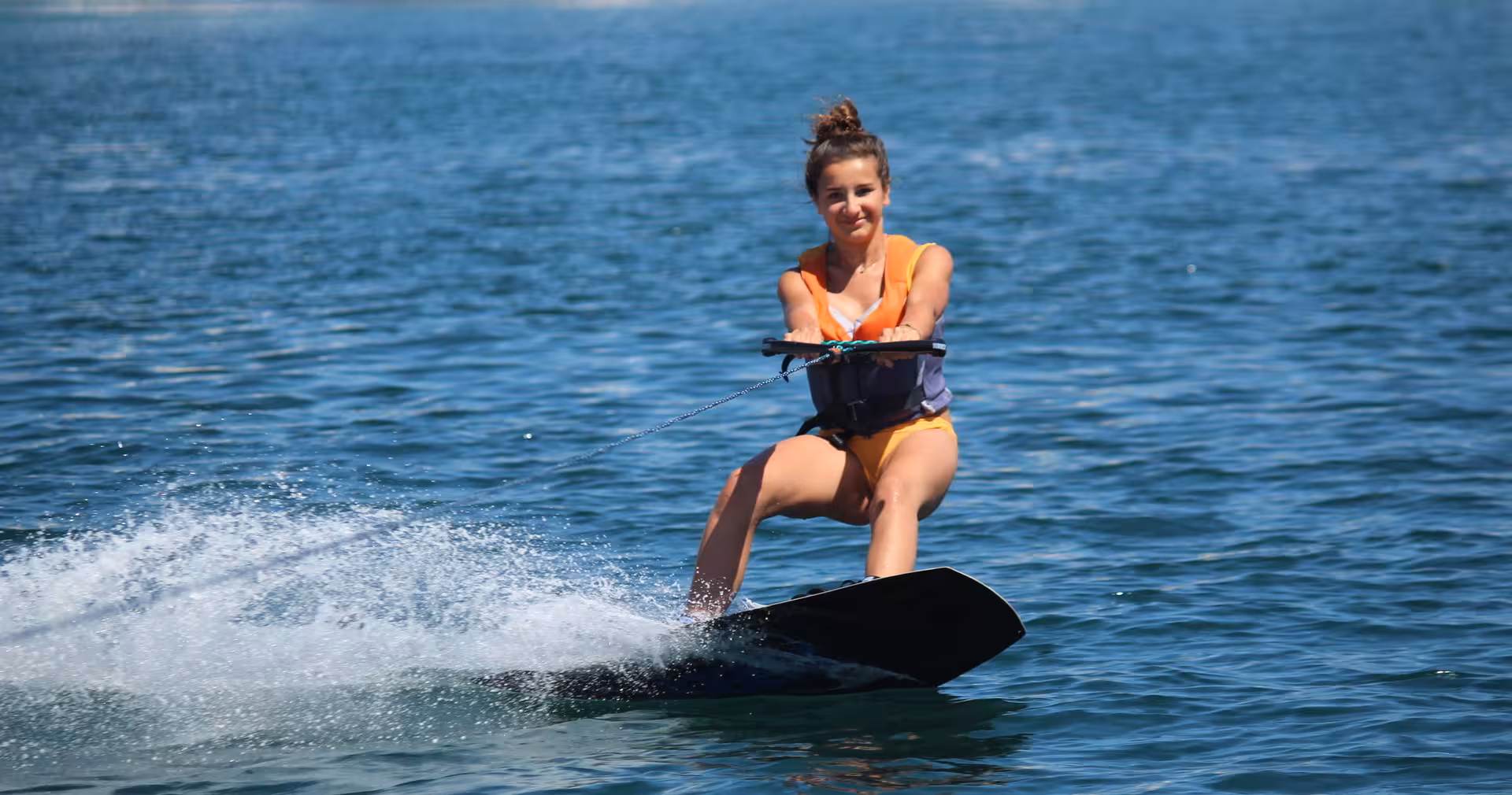 A smiling girl wakeboarding on calm blue sea during a beginner wakeboard lesson in Armacao de Pera