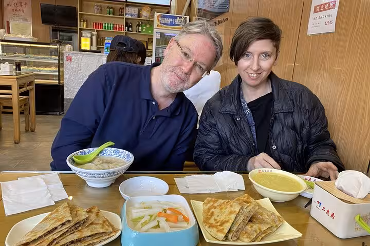 Couple enjoying traditional Beijing pancakes and local dishes at a cozy restaurant during a sidecar food tour.