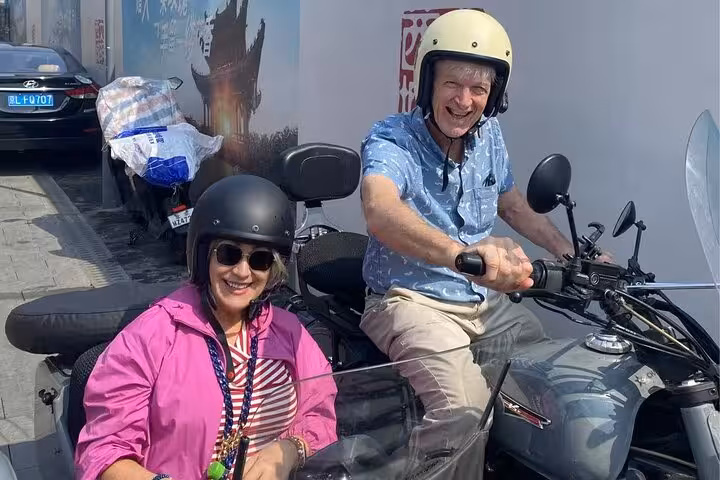 Couple in helmets smiling on a sidecar during the Beijing food tour, experiencing the city's sights and tastes firsthand.