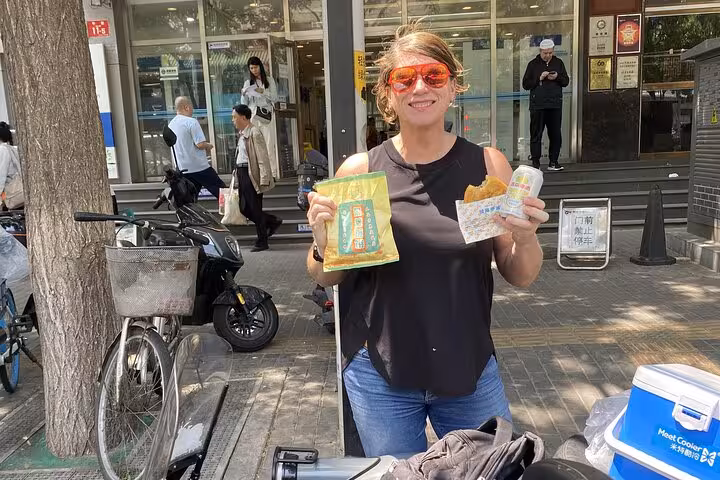 A participant on the Beijing food tour holds local snacks and drinks, showcasing the culinary delights of the city.