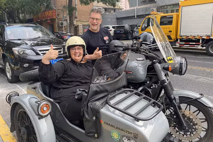 Smiling riders give thumbs up during a Beijing sidecar tour through bustling city streets.