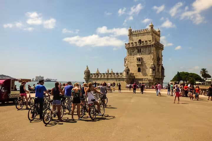 Cyclists gather near the iconic Belém Tower under a clear blue sky during a private bike tour in Lisbon, Portugal.