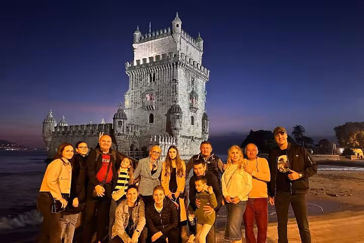 Visitors posing in front of the illuminated Belém Tower at night, a highlight of the private Belém tour.