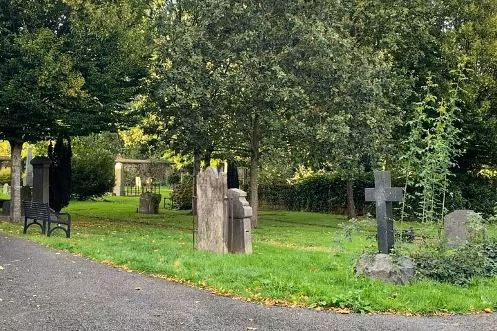 Historic gravestones and stone cross in a leafy Belfast cemetery on a ghost walking tour route