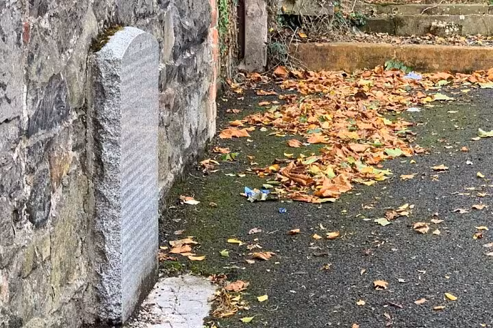 Ancient stone gravestone beside mossy wall with autumn leaves on ground in Belfast