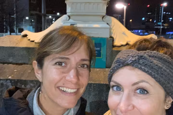 Two women smiling for a selfie at night near a snow-covered monument in Belfast