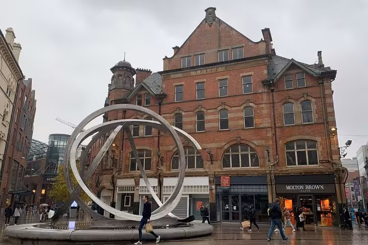 Victorian red brick building and modern circular sculpture on a rainy Belfast city street