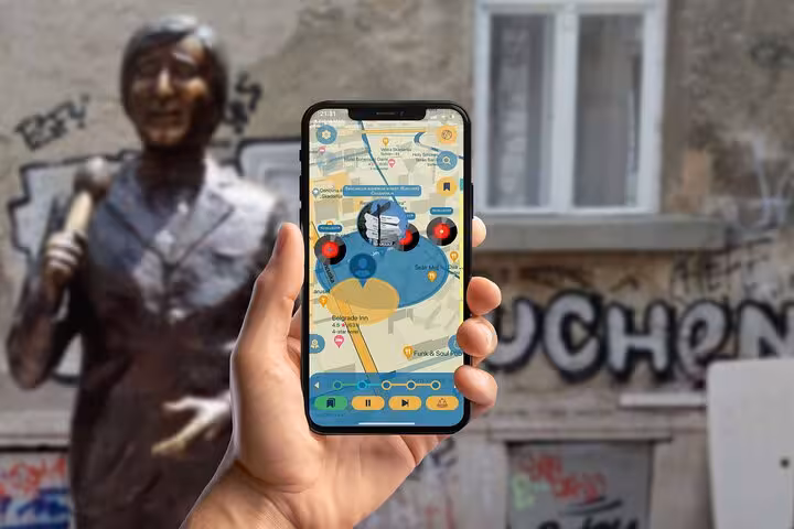 Hand holding a smartphone with a Belgrade walking tour app map near a bronze statue in downtown Belgrade.