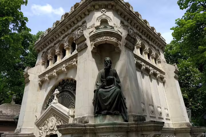 Bronze seated statue on ornate white stone mausoleum at Bellu Cemetery Bucharest surrounded by green trees
